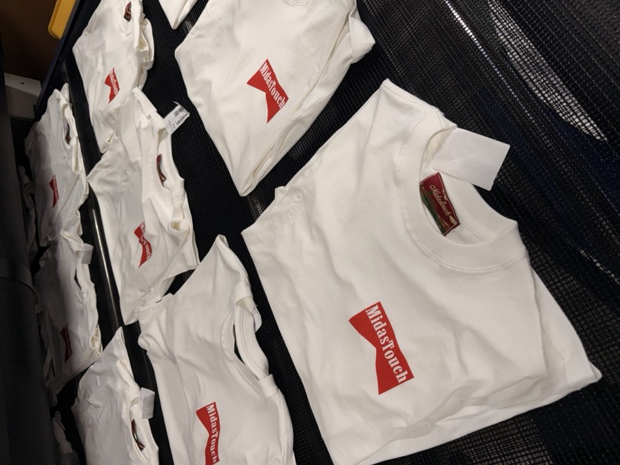 Camisetas brancas dobradas com estampa vermelha “Midas Touch”