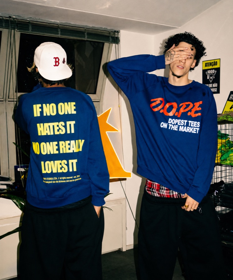 Dupla usando moletons da Dope Tees — estampa “D.O.P.E. Dopest Tees on the Market” na frente e “If no one hates it no one really loves it” nas costas