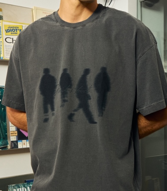 Detalhe da camiseta cinza com estampa de silhuetas caminhando e a assinatura “Midas touch”
